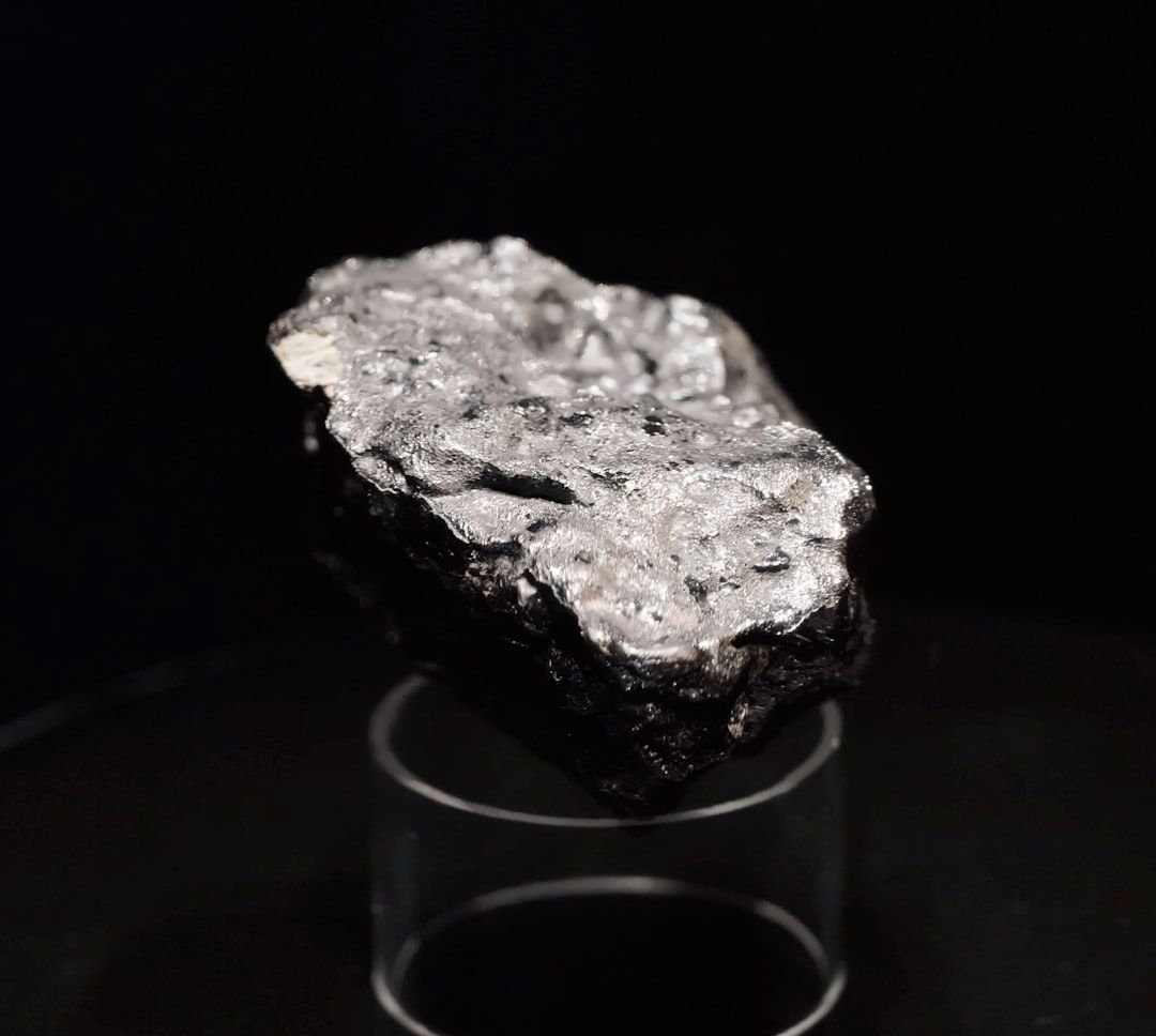En glänsande, metallisk stenbit som liknar malm eller diamantborr, stående på ett transparent stativ.